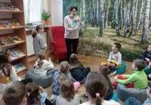Pani bibliotekarka opowiada siedzącym dzieciom o księgozbiorze