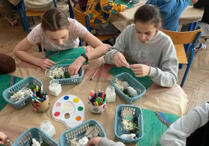uczniowie przy stolikach robią prace plastyczne