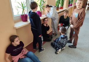 uczniowie pracują nad zadaniem - na siedząco, kilkoro na stojąco, jedna osoba coś zapisuje