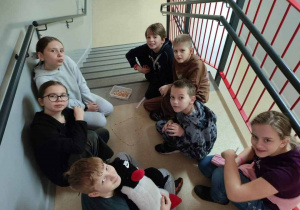 Uczniowie pozują siedząc na schodach, między nimi ułożone serduszko z koralików