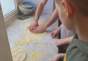 Chłopcy formują placki pod pizzę na stole obsypanym mąką