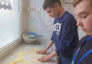 Chłopcy formują placki pod pizzę na stole obsypanym mąką