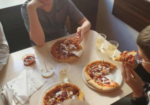 Trzy osoby przy stole przed nimi upieczona pizza
