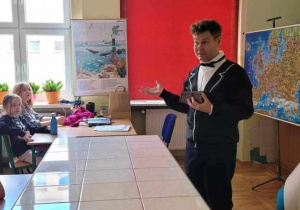 Pan prof. Chaos mówi do uczniów stojac za biurkiem