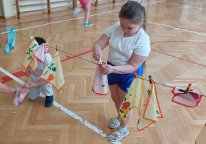 Dziewczynka przypina chusteczkę do sznura klamerkami do bielizny