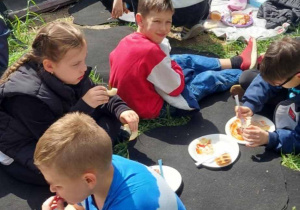 Dzieci na kocach spożywają posiłek