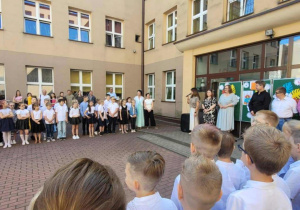 Uczniowie i nauczyciele na tle budynku szkoły