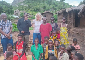 Pani Doktor w otoczeniu dzieci na tle chat i w oddali gór