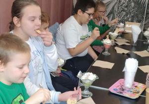 Uczniowie przed pucharkami z lodami i deserami jedzą ze smakiem