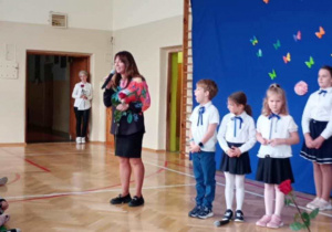 Przemówienie p. Dyrektor stojącej na tle dekoracji i odświętnie ubranych uczniów