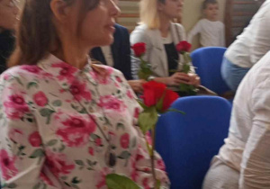 Nauczycielka w kwiecistej bluzce i z różą w dłoni