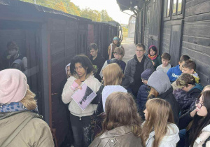 Uczniowie przy wagonie słuchają wypowiedzi przewodniczki