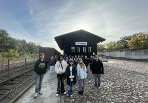 Uczniowie idący wzdłuż torów, w tle barak dworcowy