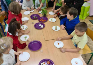 Uczniowie przy stole smakują przygotowane potrawy