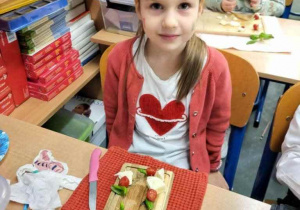 Uczennica a przed nią deska kuchenna z przygotowanym poczęstunkiem