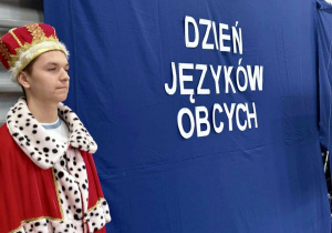 Uczeń w stroju królewskim na tle niebieskiej tkaniny z napisem Dzień Języków Obcych