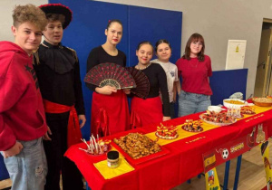 Uczniowie w strojach hiszpańskich za stoiskiem ze smakołykami tego kraju