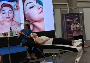 Pokaz kosmetyczny, na telebimie widać modelkę i czynności jakie wykonuje kosmetyczka