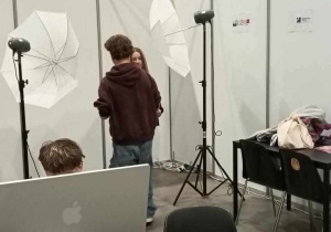 uczeń ogląda sprzęt fotograficzny, ustawione oświetlenie lamp parasolowatych jak w salonie foto