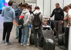 Zdjęcie grupowe - jedna osoba siedzi w bolidzie bardzo starego typu