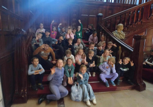 Zdjęcie grupowe uczniów obu klas siedzących na schodach pięknej klatki schodowej pałacu