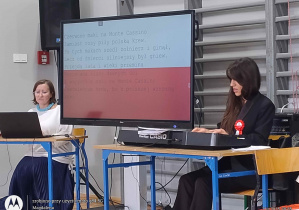 Nauczycielki na tle ekrany z barwani narodowymi i tekstem pieśni