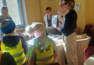 Uczniowie w żółtych odblaskowych kamizelkach obok panie Seniorki z opiekunką