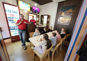 Pracownik pizzerii opowiada - dzieci siedza przy stoliku i słuchają