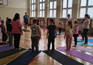 uczniowie i rodzice w sali gimnastycznej stoją w kole, za nimi karimaty