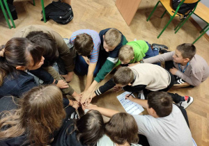 wszystkie ręce na pokład - grupa w przygotowaniu do radosnego okrzyku - dłonie siedzących w kręgu uczniów wyciągnięte i położone jedna na drugiej