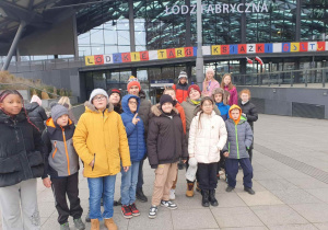Uczniowie przed budynkiem Dworca Fabrycznego, a za nimi kolorowy napis o Targach Książki