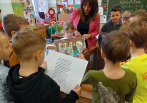 Uczniowie oglądają karty z ilustracjami i tekstem, które wkłada się do skrzyneczki teatrzyku