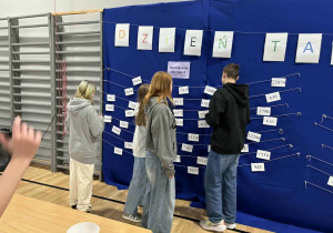 Odszukują wynik obliczanego przykładu na sznurkach przypiętych do niebieskiego materiału pod hasłem Dni Tabliczki Mnożenia