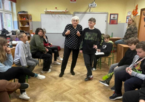 Prowadząca i uczeń rozmawiają, przed nimi na podłodze ponaklejane równolegle białe paski