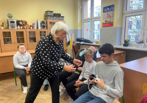 Prowadząca podaje siedzacemu uczniowi ciśnieniomierz