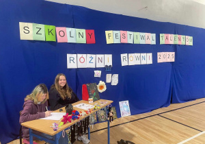 Uczennice siedzą na tle dekoracji z napisem szkolny festiwal talentów