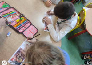 Uczniowie kolorujący obrazki na kartkach pocztowych