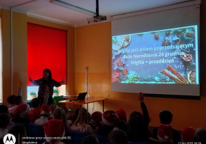 Prezentacja multimedialna i p. Dyrektor opowiadajaca o tradycjach i zwyczajach świątecznych, w tle czerwonej rolety
