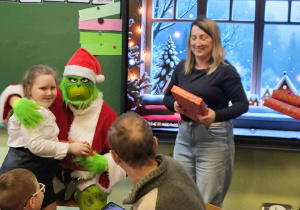 Mikołaj Grinch Pozuje do zdjęcia z dziewczynką odbierającą prezent