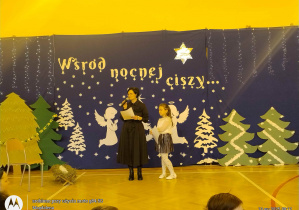 Konferansjerka wraz z uczennicą zapraszają na przedstawienie.