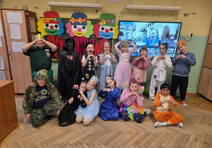 Zdjęcie przebranych uczniów na tle dekoracji - kolorowych clownów i tablicy multimedialnej