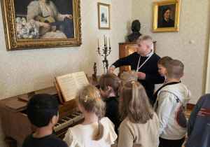 w pokoju z fortepianem, na ścianie obraz przedstawiajacy kobietę grajacą na mandolinie