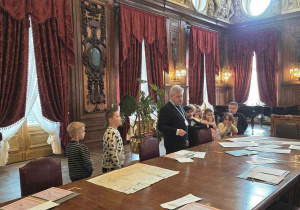 W sali spotkań dawnych przedsiębiorców, piękne rzeźbione sztukaterie, ciężkie bordowe, misternie upięte zasłony i długi prosty stó z archiwalnymi dokumentami