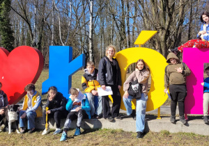 Piechurzy odpoczywają siedząc lub stojąc na tle kolorowego napisu kocham Łódź