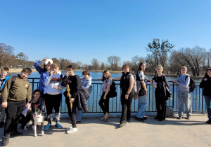 Uczniowie, uczestnicy rajdu, ustawieni rzędem na tle jeziora i blękitnego nieba