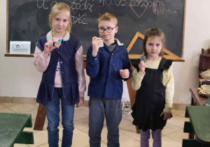 Troje uczniów prezentuje dawne mundurki szkolne