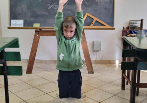 Uczeń pokazuje dawne szkolne kary, klęczy z rękami podniesionymi do góry