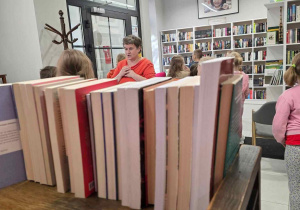 Półka z książkami, a za nimi nauczycielka i uczniowie