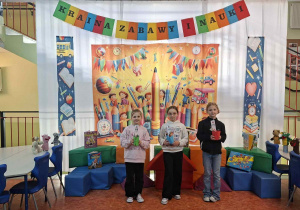 Dekoracja na holu głównym - materiał z kolorowym nadrukiem, uczniowie na jego tle, obok niebieskie pufy