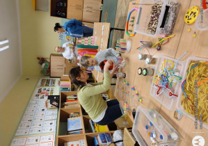 Nauczycielka pokazuje dziecku różne sensoryczne zabawy, na stolikach poukładane liczne pomoce terapeutyczne